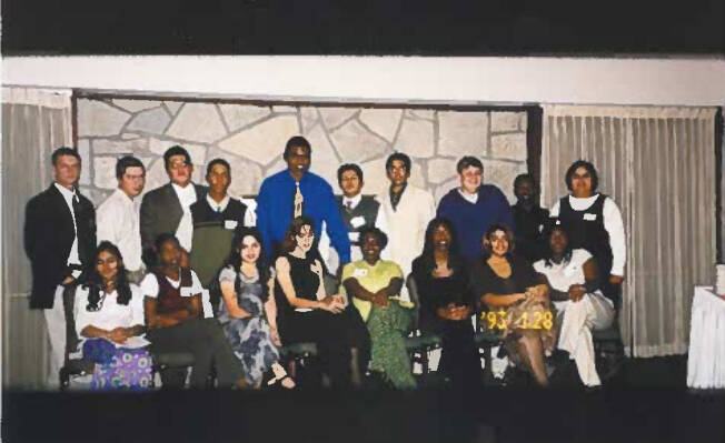 Students in two rows, with the first row sitting down and second row standing in the back, facing camera and smiling.